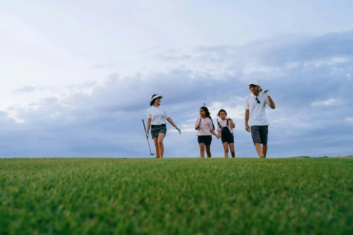 Family walking on a grassy hill with golf clubs